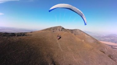 Bir FPV kuadkopterinde çekildi. Güneşli bir günde alçak bir dağın yanında yamaç paraşütü yapan bir sporcu uçar. Hava görüntüsü Adrenalin Konsepti, İHA Atışı.