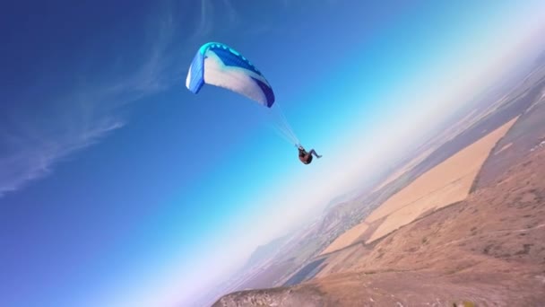 スポーツFpvクワッドコプターで撮影 パラグライダーのアスリートは 低い山の隣で晴れた日に飛ぶ アリアルビューアドレナリンコンセプト ドローンショット — ストック動画