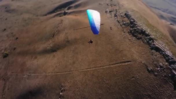 スポーツFpvクワッドコプターで撮影 パラグライダーのアスリートは 低い山の隣で晴れた日に飛ぶ アリアルビューアドレナリンコンセプト ドローンショット — ストック動画