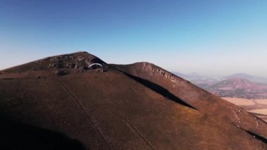 Bir paraşütçü, tarlalardan havalandıktan sonra toprağın üzerinde hafifçe süzülür. Bir paraglider hava akımında hızlı hareket eder, İHA 'dan çekim yapar.