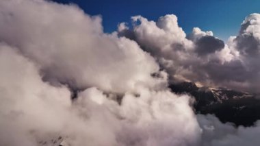 Kardaki volkanik dağların havadan görünüşü. Güneş batarken uçan kabarık bulutların arasından bir dron geçiyor, 4K.