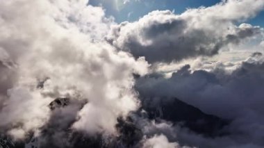 Kardaki volkanik dağların havadan görünüşü. Güneş batarken uçan kabarık bulutların arasından bir dron geçiyor, 4K.