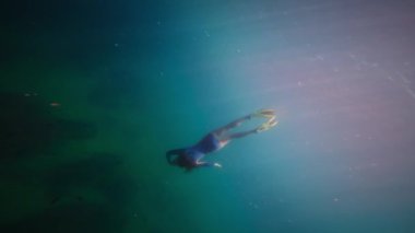 Genç beyaz kadın su altında şnorkelle yüzüyor. Yüzgeç maskesi ve şnorkel suyun altında yüzmene yardımcı olur. Yavaş çekim.