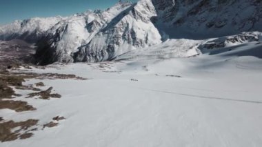 Bir FPV İHA 'sı kar yığınının üzerinden uçuyor, sonra da serbest bir grubun üzerinden. Kayak sporcusu, hava manzaralı, açık hava hobisi 4k.