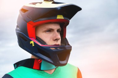 Kendine güvenen yakışıklı bir sporcunun yakın plan portresi şık bir kaskla kameraya bakıyor kararlılıkla, açık havada bir yaz günü yarışmaya hazır..