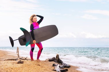Genç bir kadın deniz kıyısında su sporu yapmak için yürüyor. Hidrofolyo sörfü. Elinde hidrofolyo tutan seksi sporcu kadın..