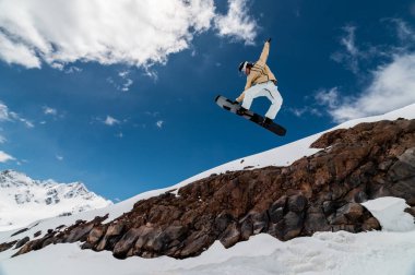 Profesyonel snowboardcu vurucudan yükseğe zıplıyor, uçan eliyle tahtayı tutuyor..