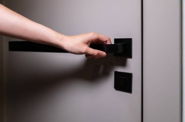 Tanınmayan bir kadın elini modern bir kapıya uzatıyor ve odayı açmak için siyah bir kapı kolu kullanıyor..