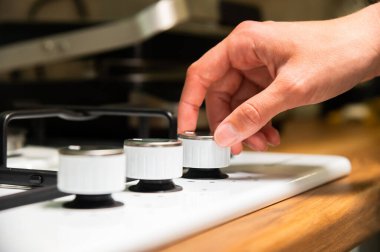 Bir kadın eli, seçiciyi gaz sobasında döndürür. Kadınların elleri gaz sobasının ocağını yakar..