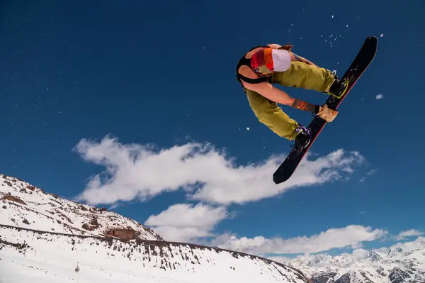 stock image Young professional snowboarder rides big air in big mountain snow park, sliding and splashing snow in sunny winter.