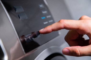 Çamaşır makinesine basarken bir elin parmağı ile program seçerken yakın plan görüntüsü.
