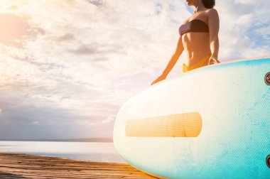 Bikinili mutlu sağlıklı bir kadın sahilde sörf tahtasıyla rahatlar, turkuaz deniz suyunda yüzmeye gider. Sağlık sporları. Yaz eğlencesi, tatil seyahati.