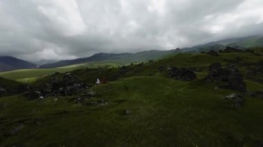 Dağların üzerinden uçmak ve insanların yürüyüş sonrası dinlenmesi, taşlı güzel yeşil bir alan. Drone FPV atışı, 4K.