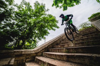 Bisikletli bir erkek Freerider hızla şehir merdivenlerinden iner. Ağaçların arasındaki eski bir merdivenden bir dağ bisikletiyle hızlı bir iniş, panoramik manzara..