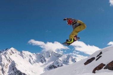 Genç kadın snowboardcu karlı dağlarda sıçrama tahtasından atlıyor..