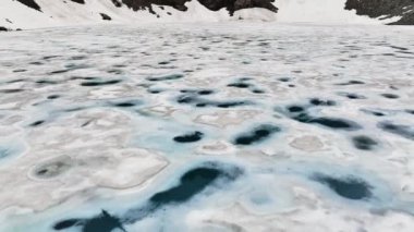 Karla kaplı dağlar ve buz parçalarıyla sakin bir göl manzarası. İnsansız hava aracı gölün üstünde, hava manzaralı...