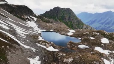 Bir çığ tarafından vurulan bir dağlık göl. Bulutlu bir günde dağların zirveleriyle çevrili yerel dağlık bir göl. AERİAL görüntüleme.