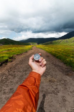 Bir dağ yolunun arka planına karşı elinde pusula, dikey fotoğraf. Seyahat ve yürüyüş için bir yol seçiyorum..