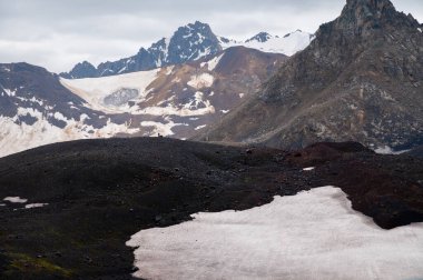 Görkemli bir dağın eteğindeki erkek turist figürü. İzlanda 'nın cansız volkanik dağ manzarası. Keskin antik bir dağ olan karlı ve buzullu alanlar..
