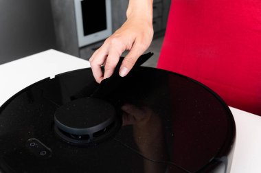 Akıllı bir robot elektrik süpürgesinin bakımı. Kadınların elleri yuvarlak bir robot elektrik süpürgesinin bakımını ve temizliğini yapar. Bir ev temizleyicisinin kesintisiz çalışması.