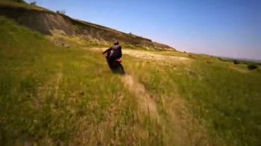 FPV İHA motorsiklet sürücüsünün dönüşünü ve off-road atlayışını yakalıyor. Sahada heyecan verici hareketler ve dublörler.