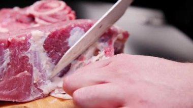 Mutfak masasındaki tahtada bıçakla çiğ domuz eti kesen bir adamın yakın çekim elleri..