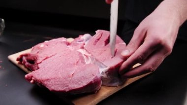 Elleri bıçaklı, ahşap kesme tahtasıyla çiğ et kesen siyah arka planda, yakın plan. Izgara et hazırlanıyor..