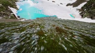 FPV İHA yüksek irtifa alp gölü üzerinde alçaktan uçar. Turkuaz bir buzul gölü suyu ve yüksek irtifa manzarası. Bir spor kuadkopteriyle vurulmuş..