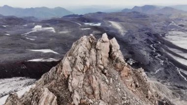 Büyük bir buzulun yanına volkanik küller serpiştirilmiş cansız tarlalarla çevrili kayalık bir dağ. İzlanda 'nın karla kaplı zirvelerinin havadan görünüşü