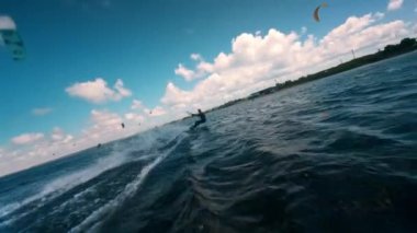 Körfezin üzerindeki bulutlu gökyüzünde uçurtma kaykayları var. Aktif spor insanları ve doğanın güzelliği. Hava sporu, yavaş çekim videosu.