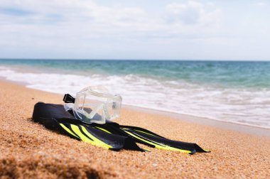 Altın deniz sahilinde bir şnorkel maskesi ve yüzgeçler yatar. Denizde şnorkelle yüzme kavramı.