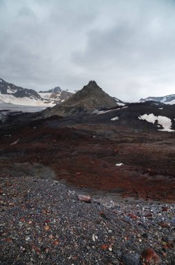 Volkanik kayalar ve buzullarla çevrili, merkezinde antik bir dağ bulunan cansız bir volkanik manzara..