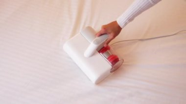 Elektrik süpürgesi ultraviyole lambalı ve tozlu karıncalardan döşekleri temizlemek için. Bir kadının eli yatak odasındaki yatağı temizleyip dezenfekte ediyor..