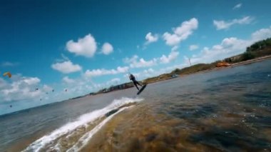 Profesyonel mutant, güzel su sıçratmaların ve harika manzaraların arka planına karşı zor bir numara sergiliyor. Dişi uçurtma sörfçüsü ağır çekimde bir numara yapıyor..