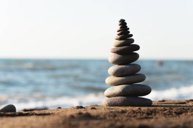 Piramit taşları kumsalın kumlarında dengelenir. Nesne odak noktasında, arkaplan bulanık. Deniz kıyısında sükunet, taş piramidinin inşasında meditasyon süreci.