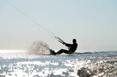 Dalgalarda sörf yapan uçurtma. Atletik adam silueti denizde uçurtma tahtasının üzerinde hızlı gidiyor, dalgalar yaratıyor ve suya su sıçratıyor..