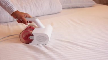 Elektrik süpürgesi ultraviyole lambalı ve tozlu karıncalardan döşekleri temizlemek için. Bir kadının eli yatak odasındaki yatağı temizleyip dezenfekte ediyor..