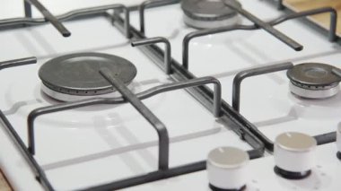 Gaz sobası mavi bir alevle yanar ve ön planda odaklı olmayan bir el düğmeyi çevirir. Konutların gazlaştırılması.