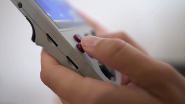 Yüzeyin derinliğine yakın çekim. Genç beyaz bir kadının ellerinde tanımlanamayan portatif retro konsol. Kız, eski konsol oyunlarına benzemek için retro oyunlar oynuyor.