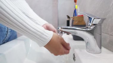 Genç bir kadının banyo lavabosuna yürüyüp ellerini yıkamasına yakın durun..