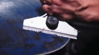 Snowboard yüzey onarım işlemi. Sığ alan derinliğiyle yakın çekim. Teknisyen snowboard 'a sürülen fazla balmumunu kazıdı.