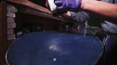 Kayak malzemeleri tamir atölyesindeki bir zanaatkarın kadın elleri. Kar kaykayının kayan yüzeyine ütüyle balmumu sürüyorum. Yakın plan. Sığ alan derinliği.