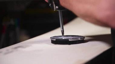 Kayak malzemeleri tamir atölyesinde bir tornavidayla snowboard bot bağlayıcısı yıkayan bir zanaatkarın erkek elleri. Yakın plan. Sığ alan derinliği.