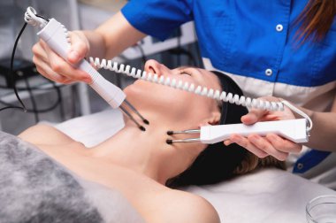 Mutlu kadın ultrasonik yüz masajı yaptırıyor. Lüks güzellik salonunda elektrikli yüz gerdirme ameliyatı olan bir kadın..