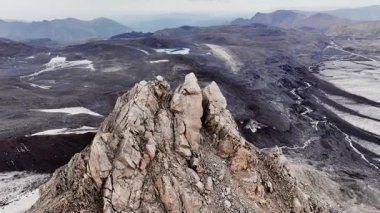 Volkanik kayalar ve buzullarla kaplı cansız arazilerdeki yüksek dağlardaki antik kayalık dağın keskin zirvesi. Hava görünümü.