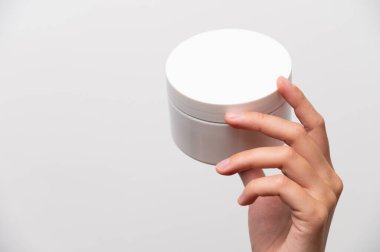 El ele tutuşan, beyaz arka planda krem rengi beyaz yüz kremi..