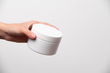 Beyaz kozmetik paketinin bir kopyası. Kadın eli beyaz arka planda yuvarlak vücut kremi kavanozunu tutuyor. Güzellik endüstrisi kavramı. Yakın plan, kopyalama alanı, afiş.