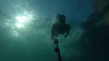 Şnorkelle yüzen bir adamın silueti ve arkadan parlayan parlak sarı güneşin arka planında selfie çeken bir adam. Güneşin zıt ışınları suyun altında dalmış bir adamın siluetini aydınlatıyor..