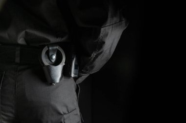 Binayı güvenlik görevlisi kontrol ediyor. Siyah arka planda, kemerinde kelepçelerle siyah üniformalı bir koruma..