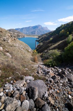Berrak bir günde dağlık kayalık arazi mavi bir göl manzaralı, dikey bir manzara.